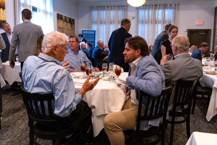 Business professionals sit around a round table at a formal reception, chatting over drinks.