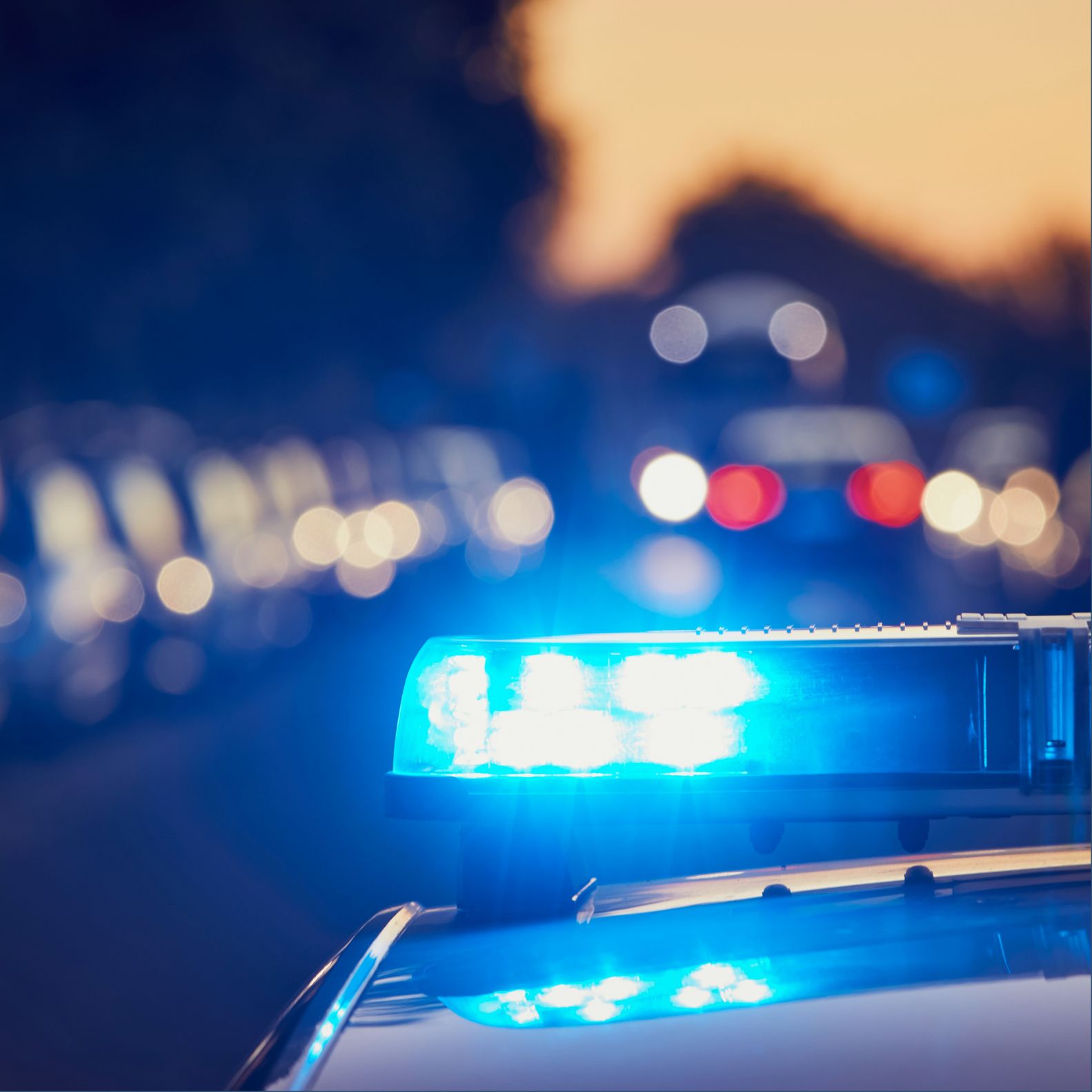 Blue police car lights flashing in the foreground with bokeh city lights in the background, at night/dusk.